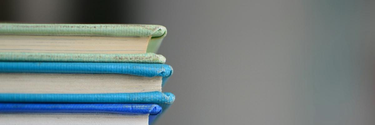 Auto-generated description: A stack of three hardcover books in shades of green and blue against a gray background.