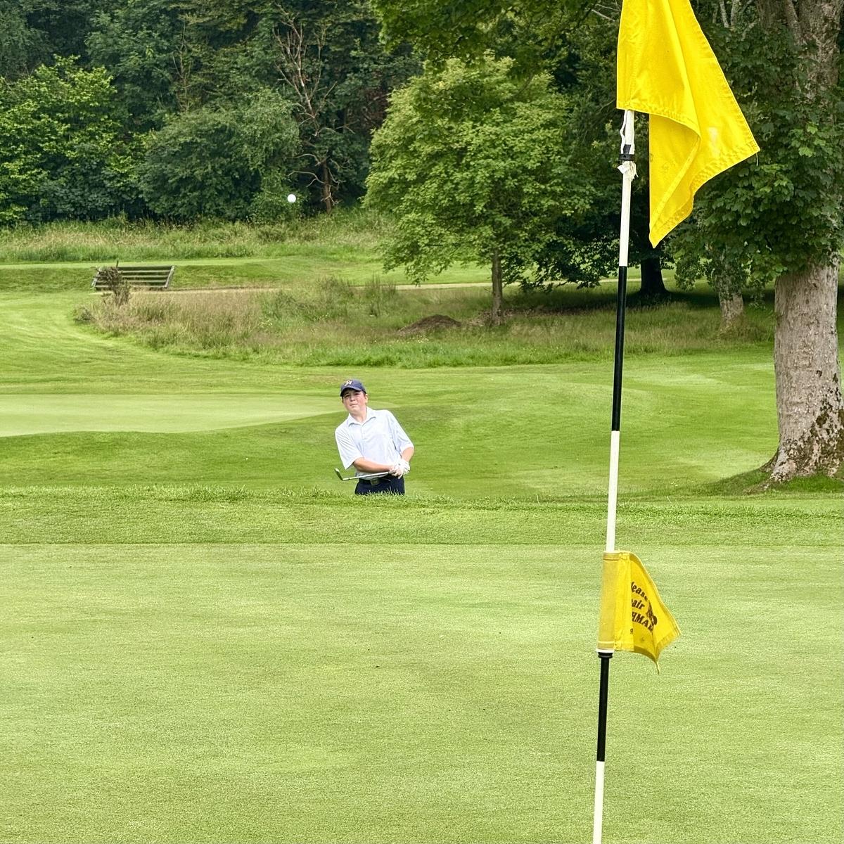 A golfer is preparing to hit a shot from a bunker on a lush green golf course near a flag.