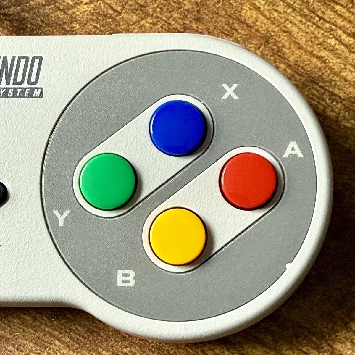 A retro gaming controller features colorful A, B, X, and Y buttons arranged in a circular pattern.