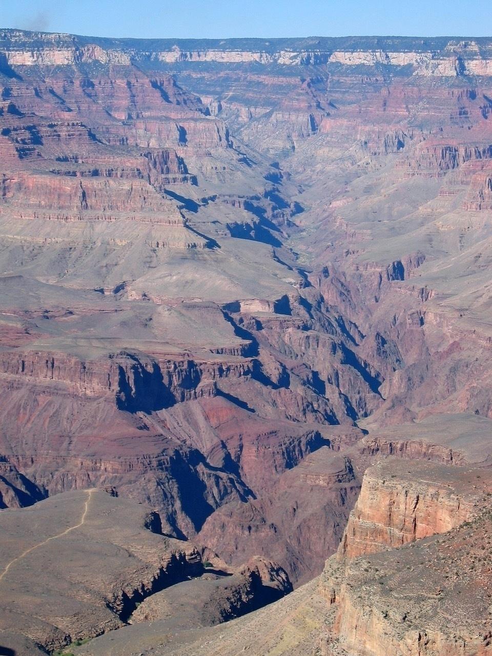 A vast and rugged canyon landscape stretches into the distance under a clear blue sky.