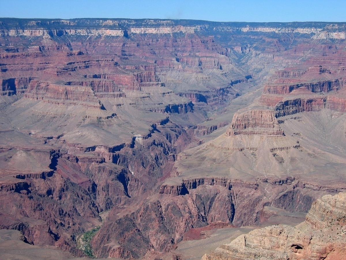 A vast, layered canyon landscape stretches out, showcasing rugged cliffs and deep valleys under a clear blue sky.