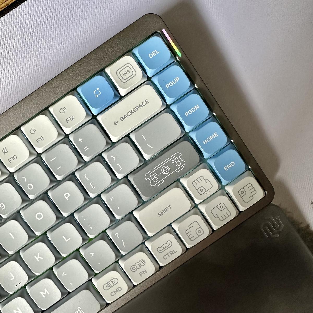 A mechanical keyboard with white, light gray, and blue keys, some of which have unique icons, is shown from an angled top view.