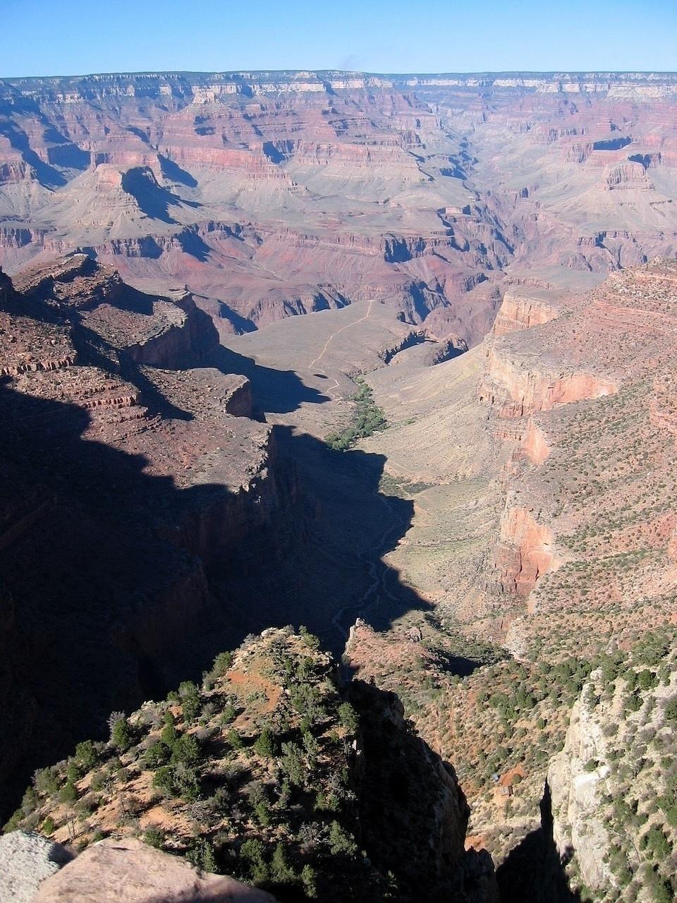 A vast canyon landscape with steep cliffs and layered rock formations stretches beneath a clear blue sky.