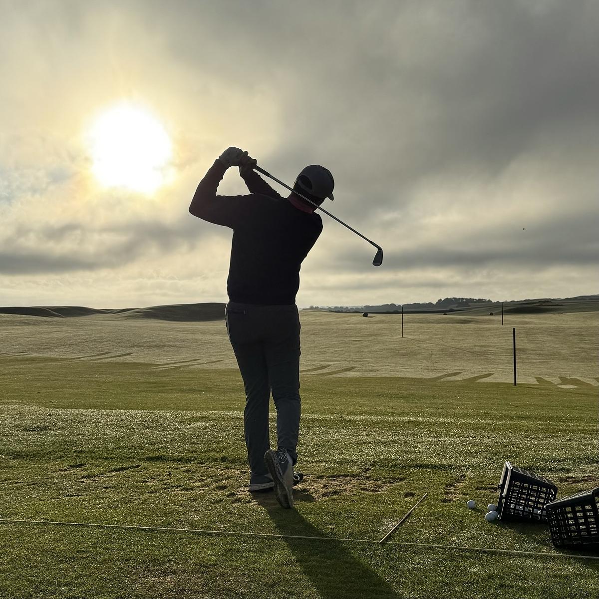 A person is swinging a golf club on a sunny day at a golf course.