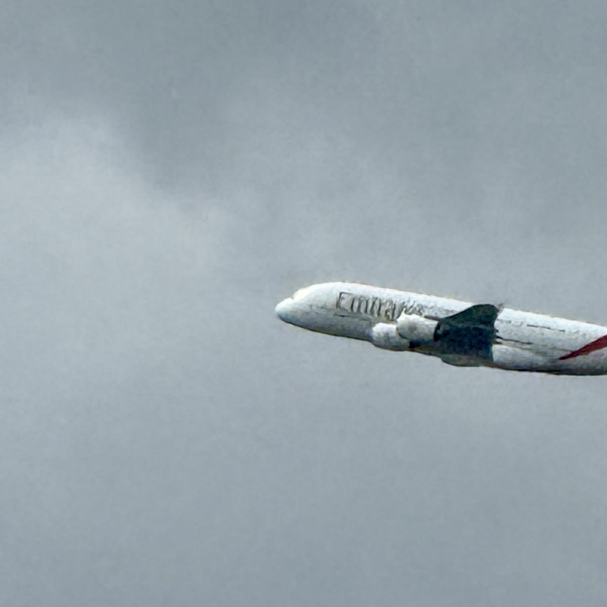 A large Emirates airplane is flying against a cloudy sky backdrop.