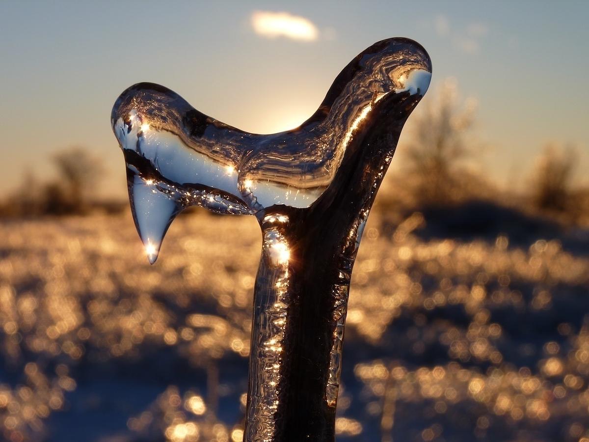 A uniquely shaped icicle glistens in the sunlight against a blurred winter landscape.