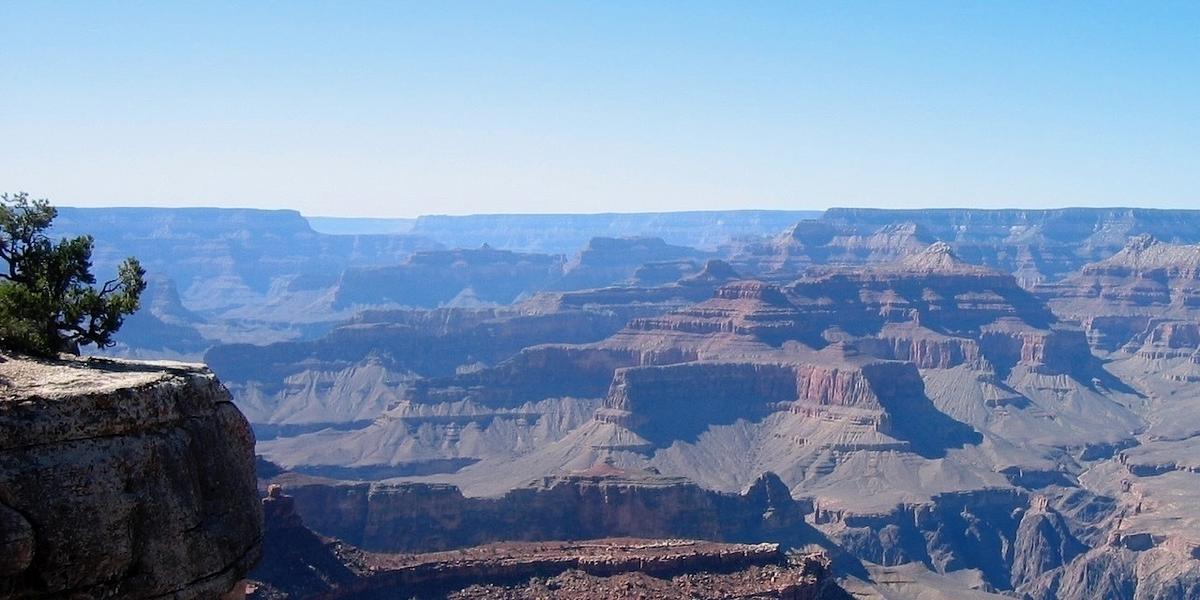 A vast landscape of the Grand Canyon is visible, showcasing layered rock formations and cliffs under a clear blue sky.