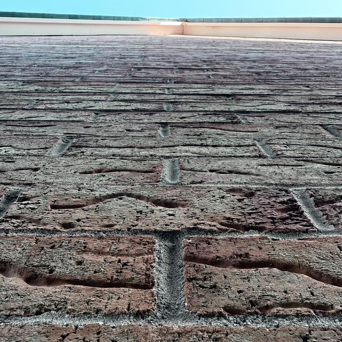 A brick wall extends upward towards a clear blue sky, viewed from a low angle.