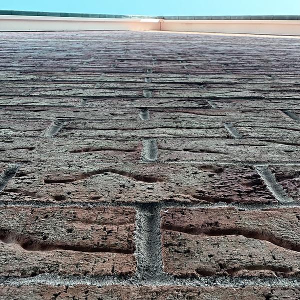 A brick wall extends upward towards a clear blue sky, viewed from a low angle.