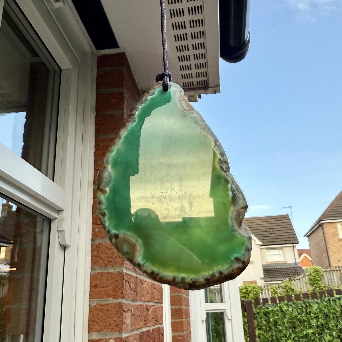 A green slice of agate is hanging in front of a brick wall with houses in the background.