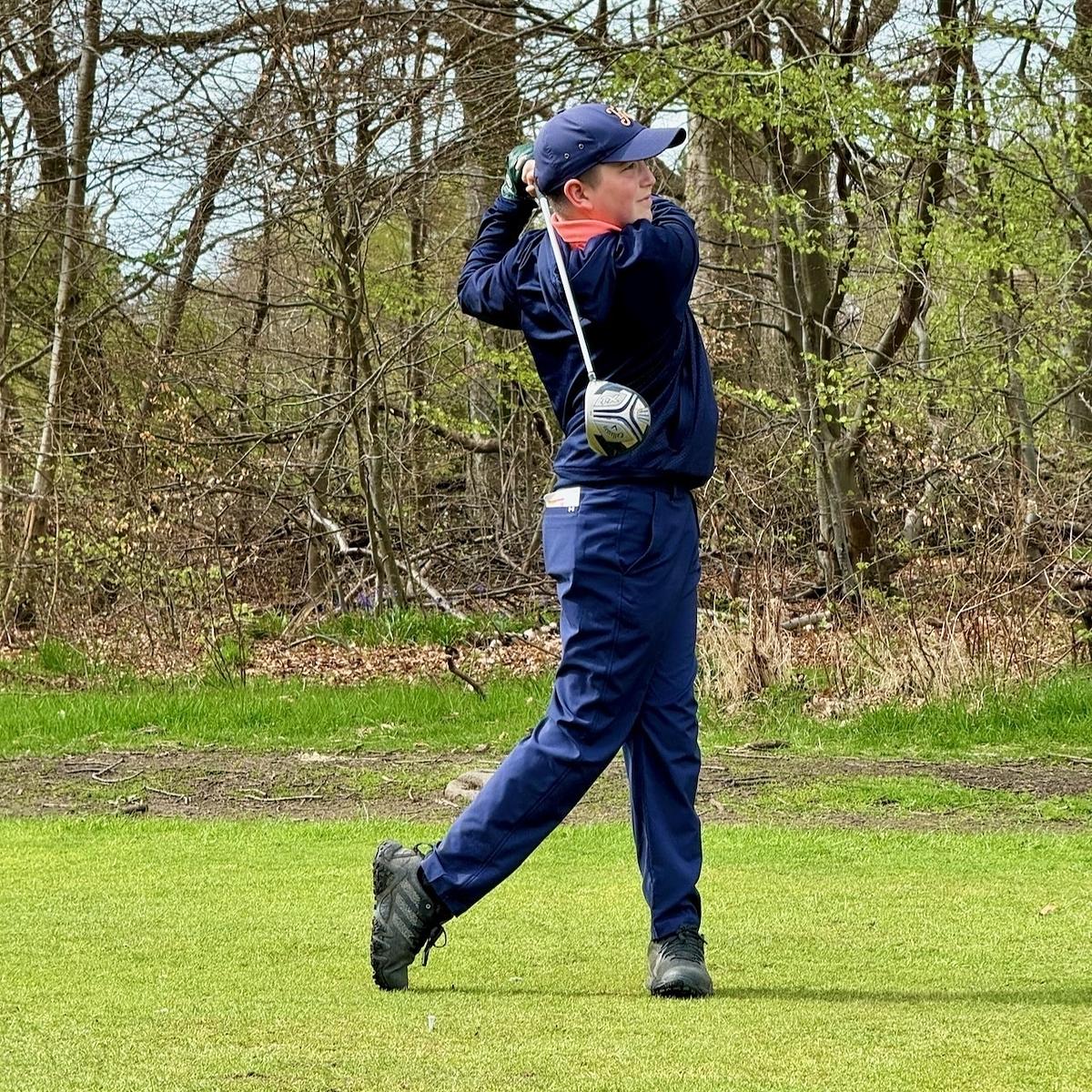 A person in a blue outfit is swinging a golf club on a grassy area surrounded by trees.