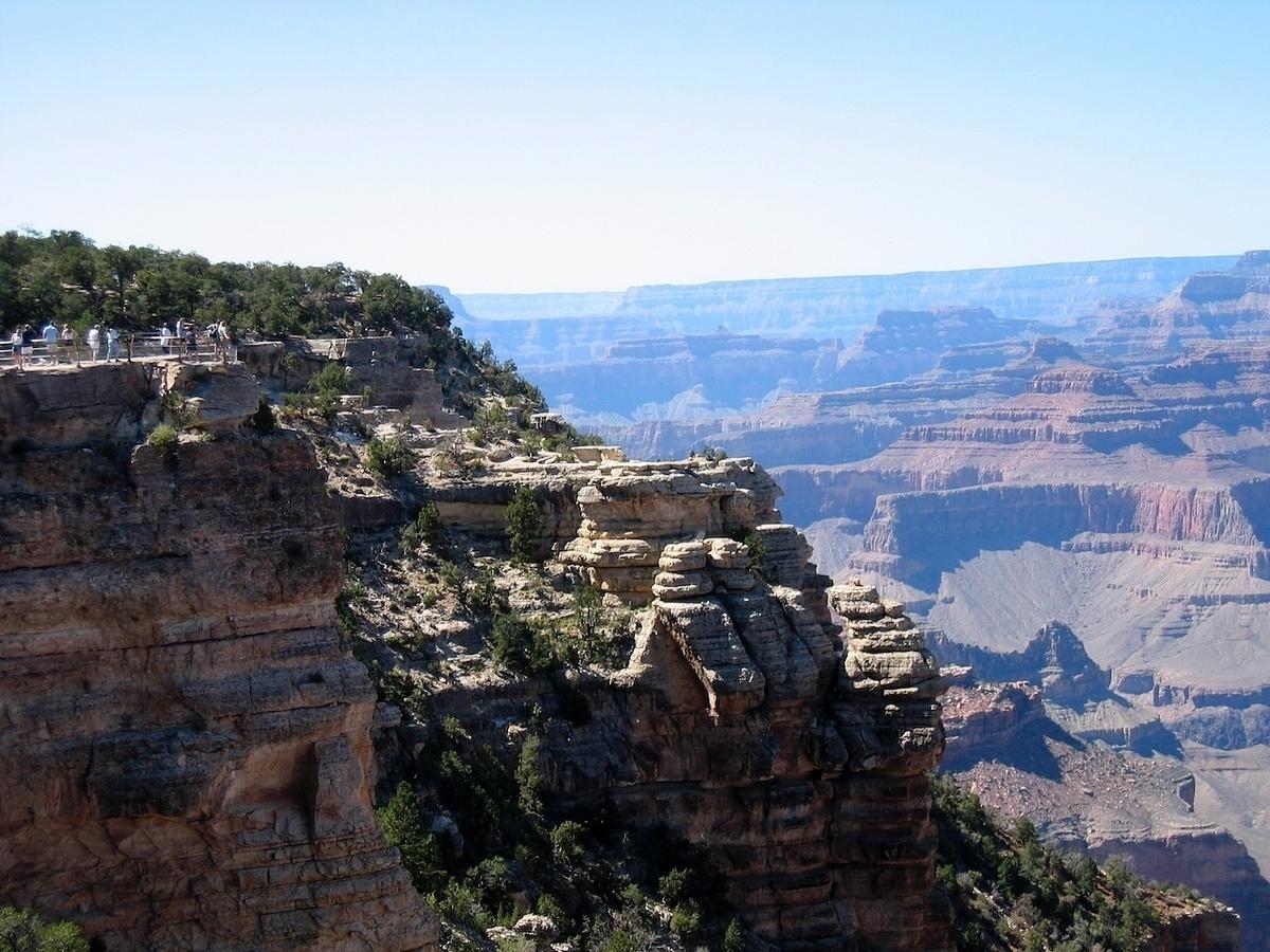 A scenic view of the Grand Canyon features layered rock formations and a vast, expansive landscape under a clear blue sky.