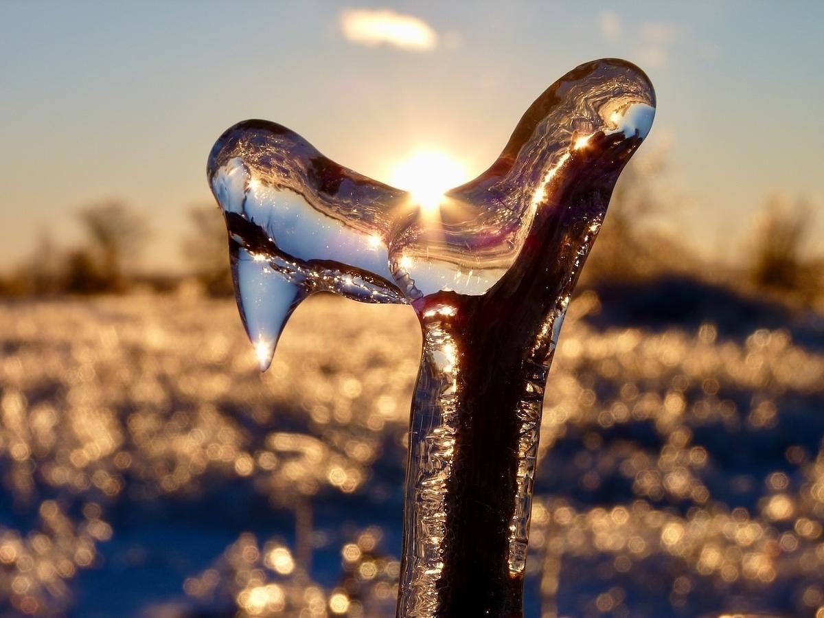 A striking scene features a beautifully illuminated icicle with the sun setting in the background, casting a warm, golden glow over a snowy landscape.