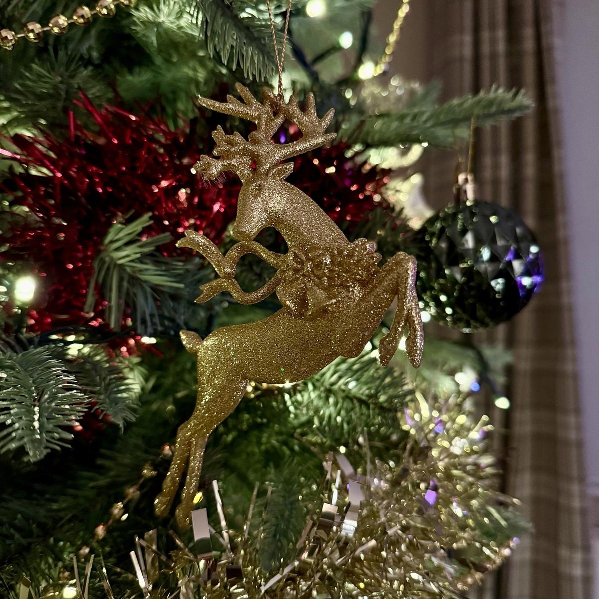 A decorated Christmas tree featuring a glittery golden reindeer ornament, surrounded by colorful tinsel and lights.