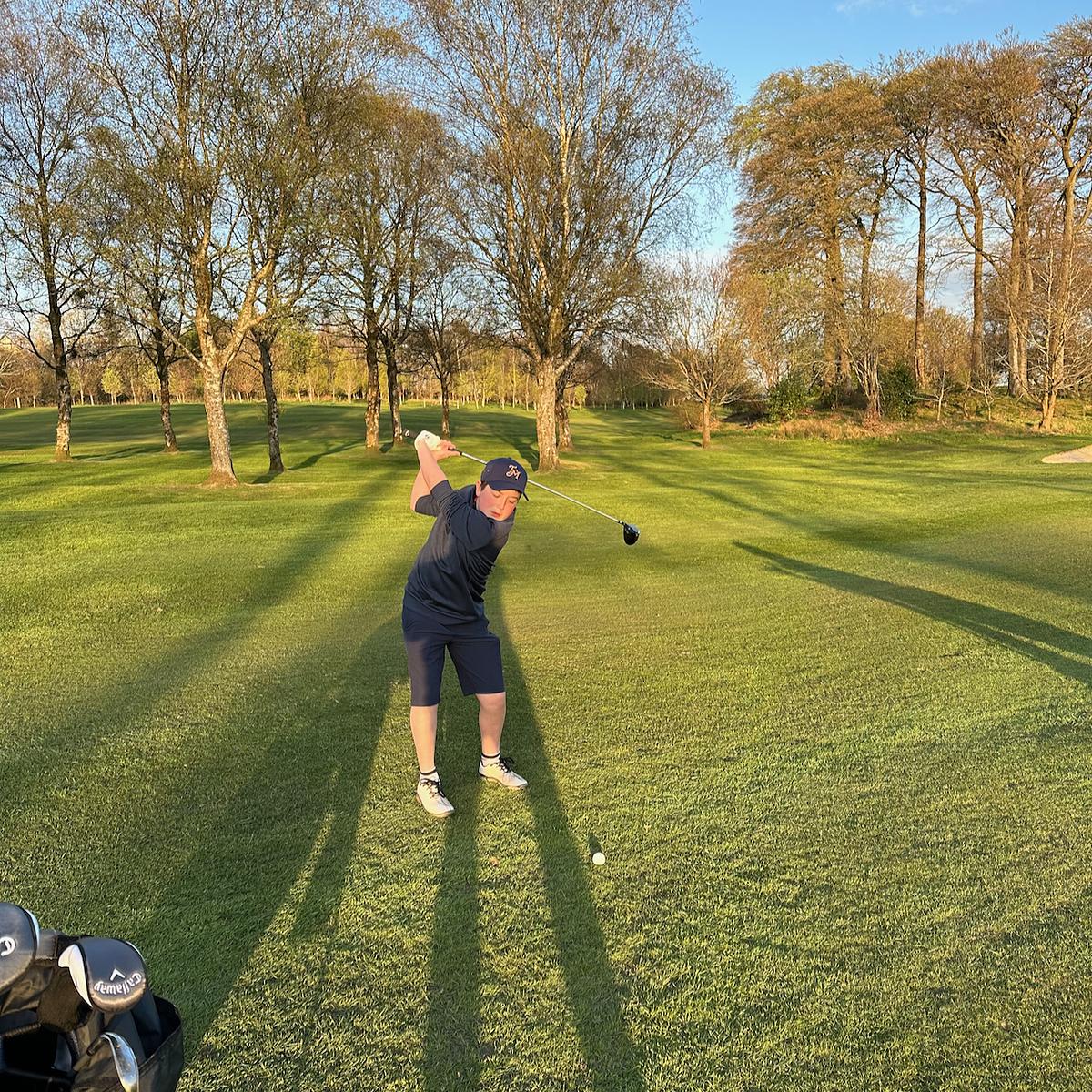 Boy playing golf with trees in the background.