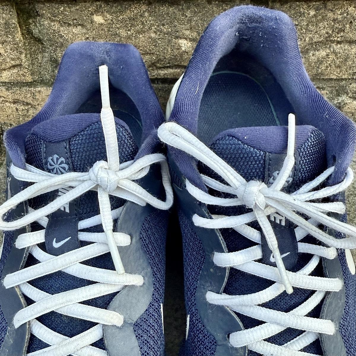 A pair of blue and white sneakers with white laces is resting against a stone wall.