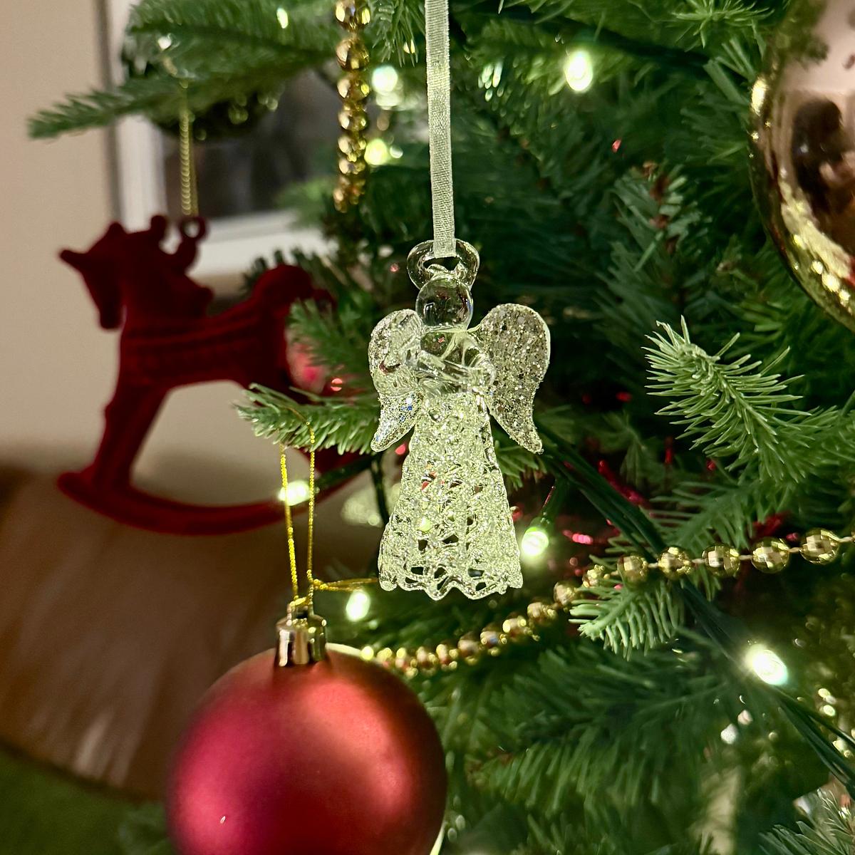 A glass angel ornament hangs on a Christmas tree decorated with red baubles, green branches, and twinkling lights.