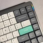 Close-up of a mechanical keyboard's upper-right corner featuring dark gray, white, and teal keycaps with an RGB light strip.